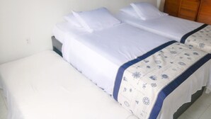 Un letto matrimoniale con biancheria da letto bianca e una coperta a motivi, un armadio in legno e un quadro blu appeso al muro.