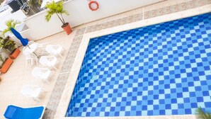 Una piscina con pavimento a scacchi, circondata da poltroncine bianche e piante in vaso.