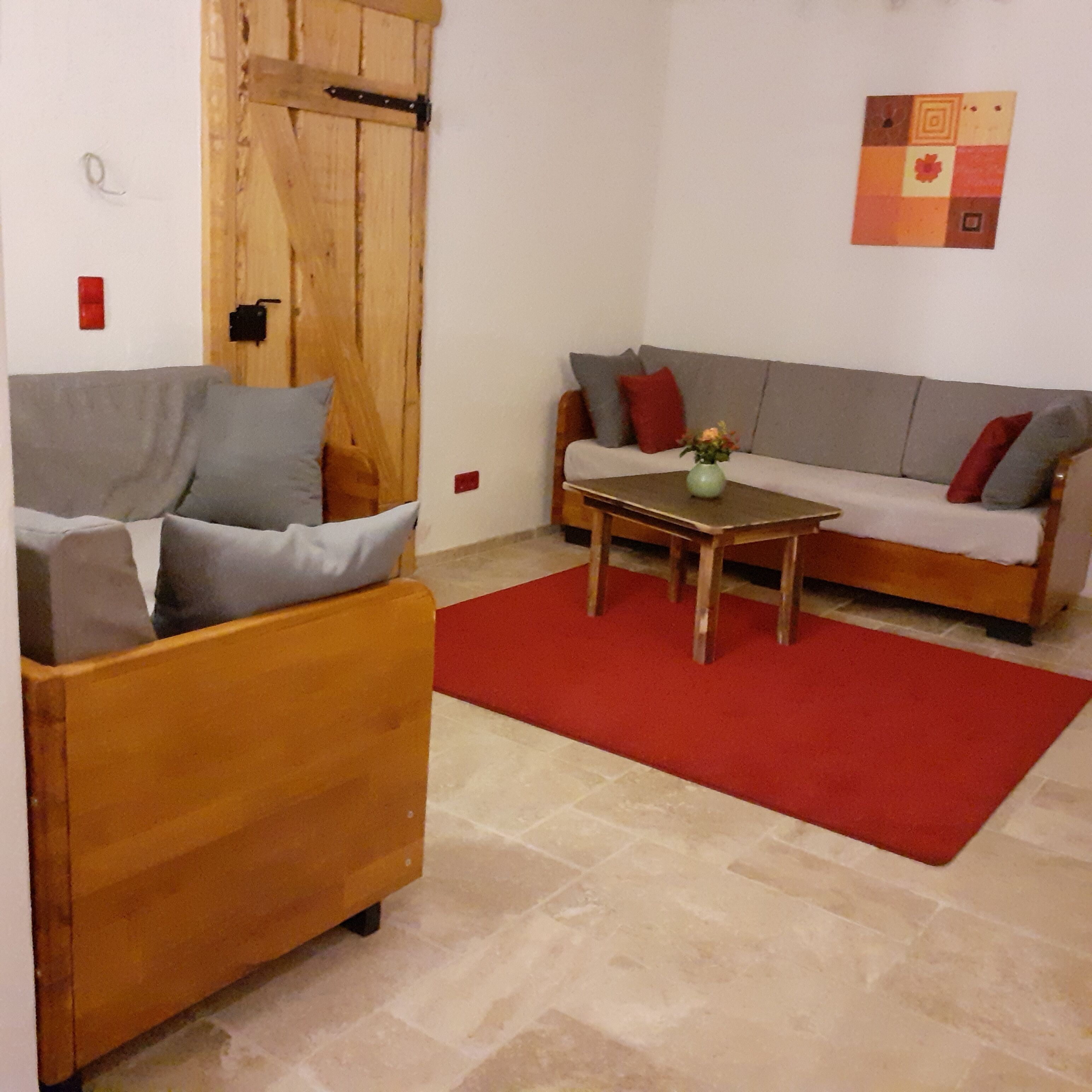 A living room with a wooden sofa, a smaller wooden armchair, a coffee table, and a red rug.
