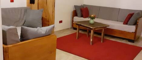 A living room with a wooden sofa, a smaller wooden armchair, a coffee table, and a red rug.