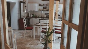 A rustic interior with a wooden ceiling, a stone floor, a dining area with white chairs, and a kitchen with white cabinets. - "Vacation cottage Plättig" (Bühlertal)