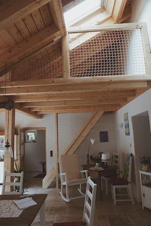 Quarto estilo loft com teto de madeira, claraboia e janela com mosquiteiro.