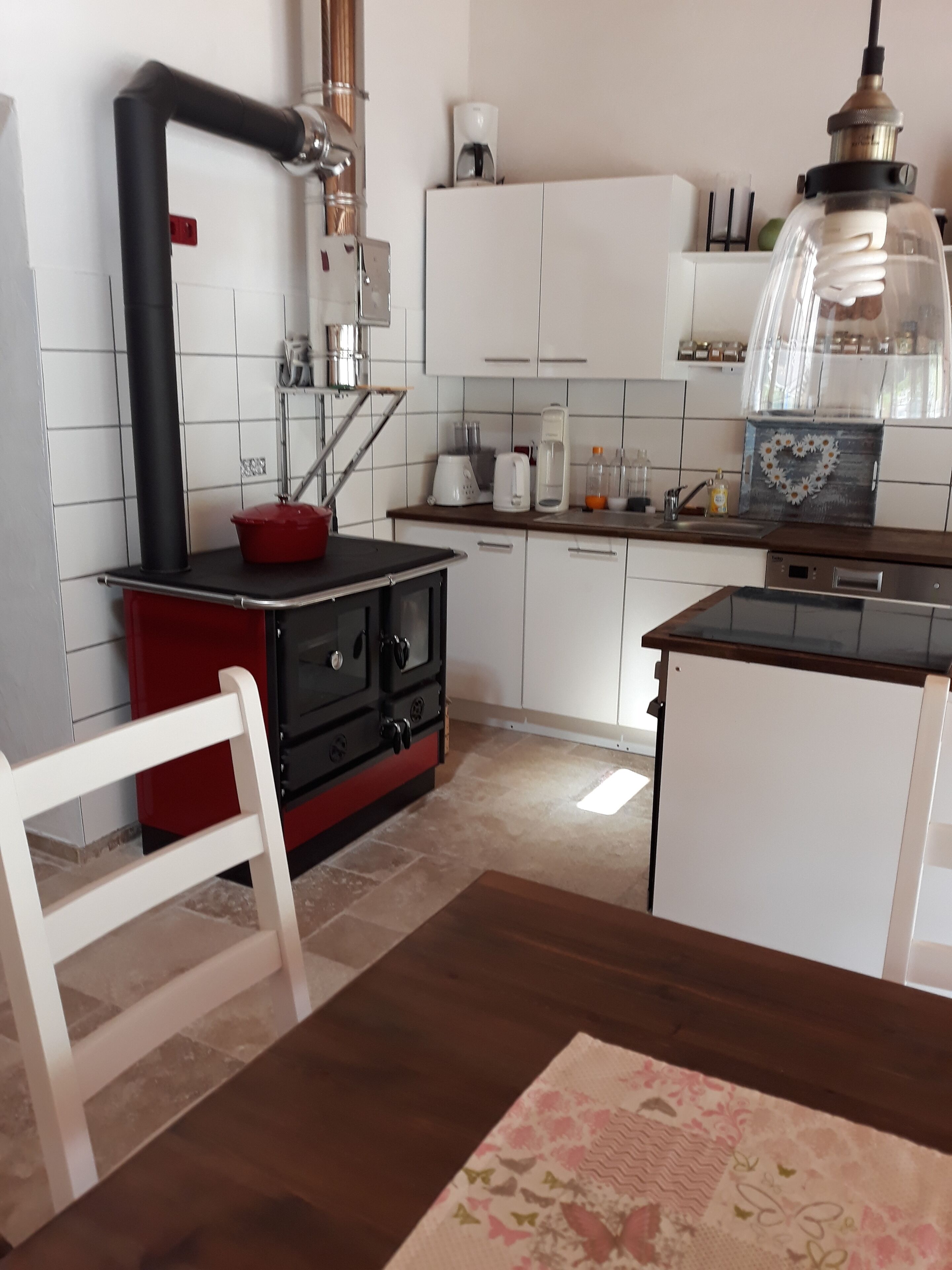 A kitchen with white cabinets, a red stove, and a wooden dining table with a floral table runner.