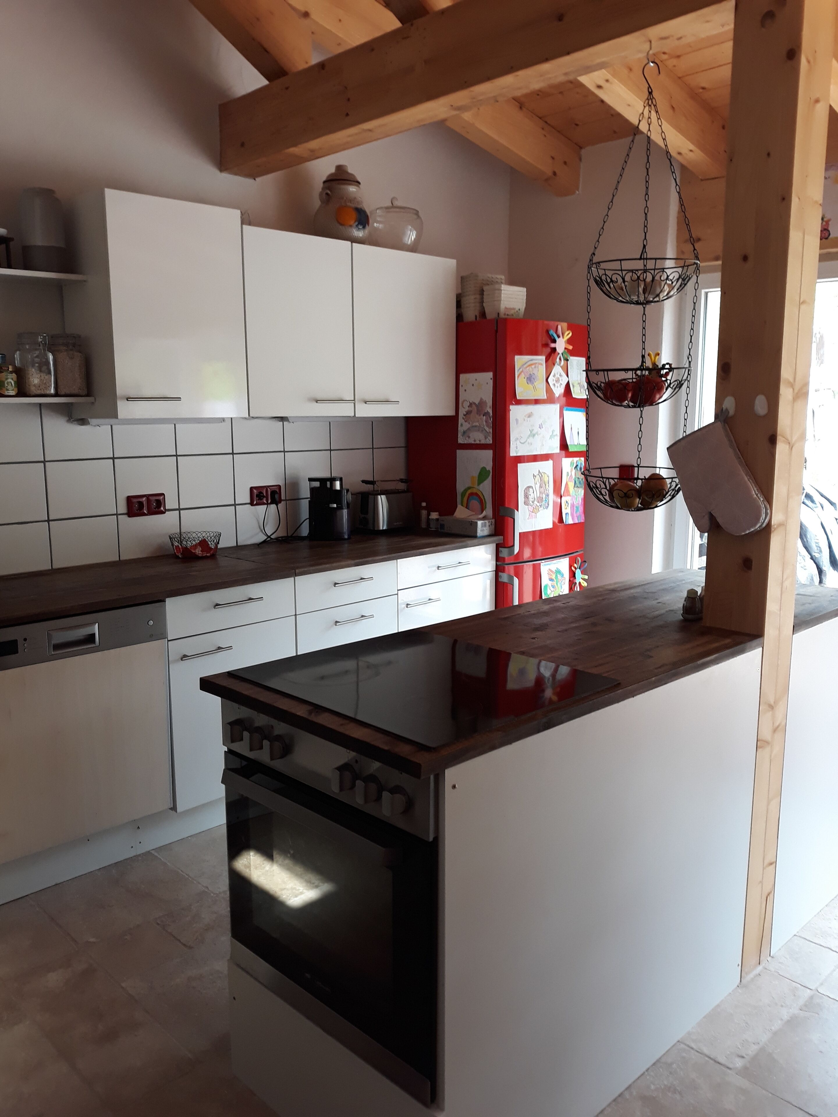 A kitchen with white cabinets, a red refrigerator, a wooden ceiling, and a hanging pot rack.