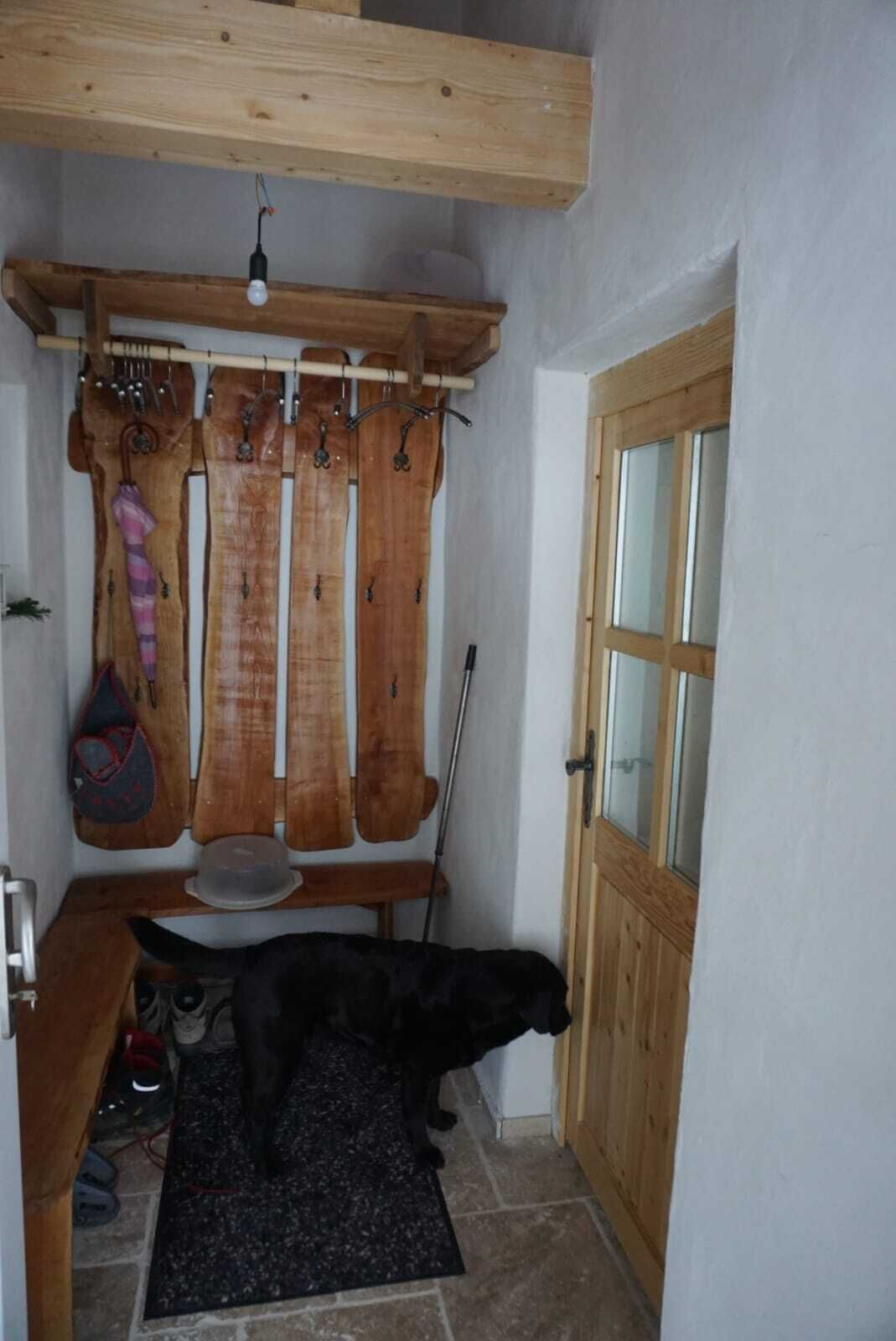 A small, rustic room with a wooden ceiling, a door with glass panels, and a black mat on the floor.