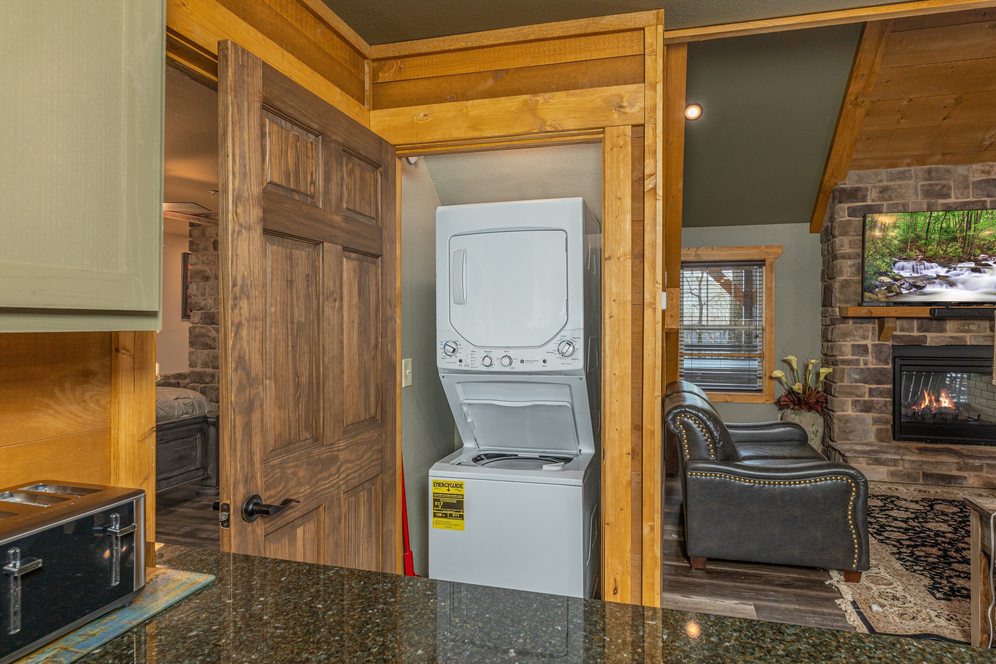 A laundry room with a front-loading washer and dryer, a wooden door, and a stone fireplace.
