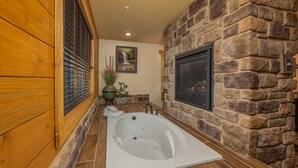 A bathroom with a stone wall, a wooden floor, a large bathtub, and a fireplace. - Beautiful Vista (Pigeon Forge)