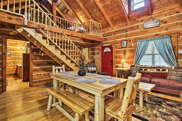 Cozy cabin interior with a central dining table, comfortable seating area, and staircase leading to an upper level.
