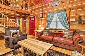 Relax in this cozy cabin-style room with a plush sofa, comfortable armchair, and wooden staircase.