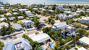 Oversigtsbillede af et kystnære boligområde med huse, en swimmingpool og en strand i baggrunden.