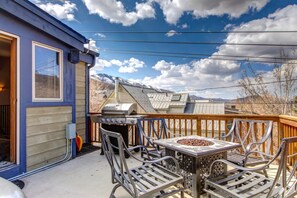 Una terraza con una parrilla y sillas de metal, con vistas a un paisaje montañoso.