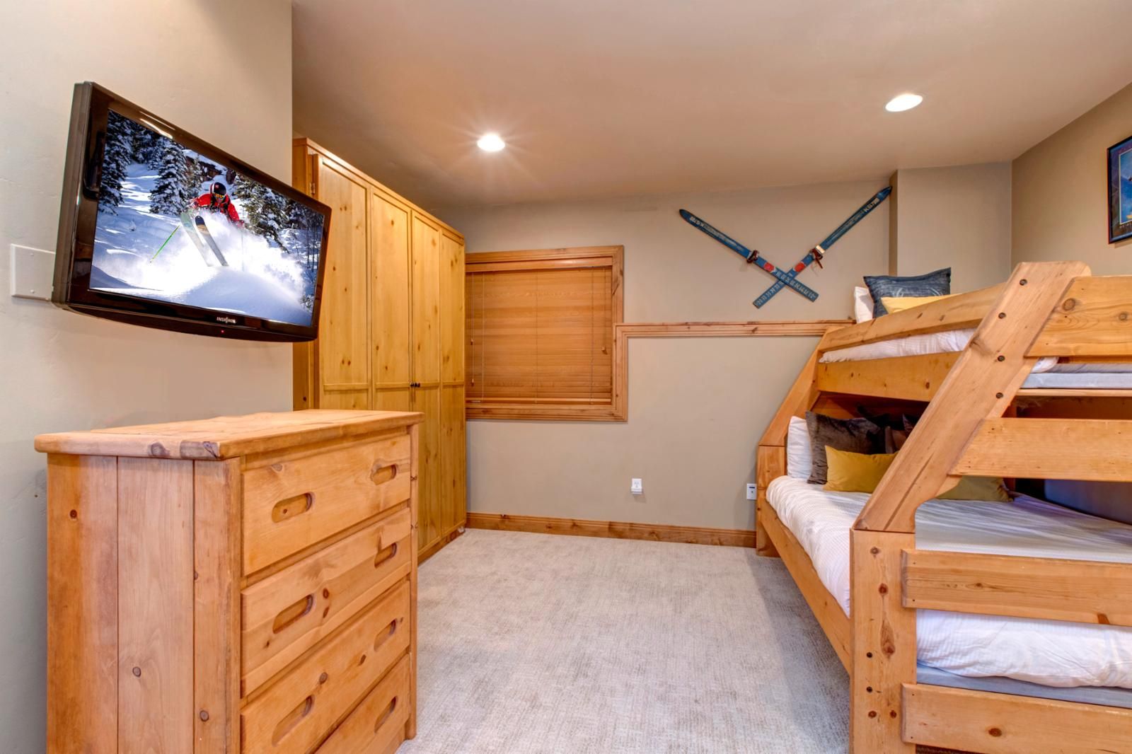 A cozy room with wooden bunk beds, a TV mounted on the wall, and a ski-themed decoration.