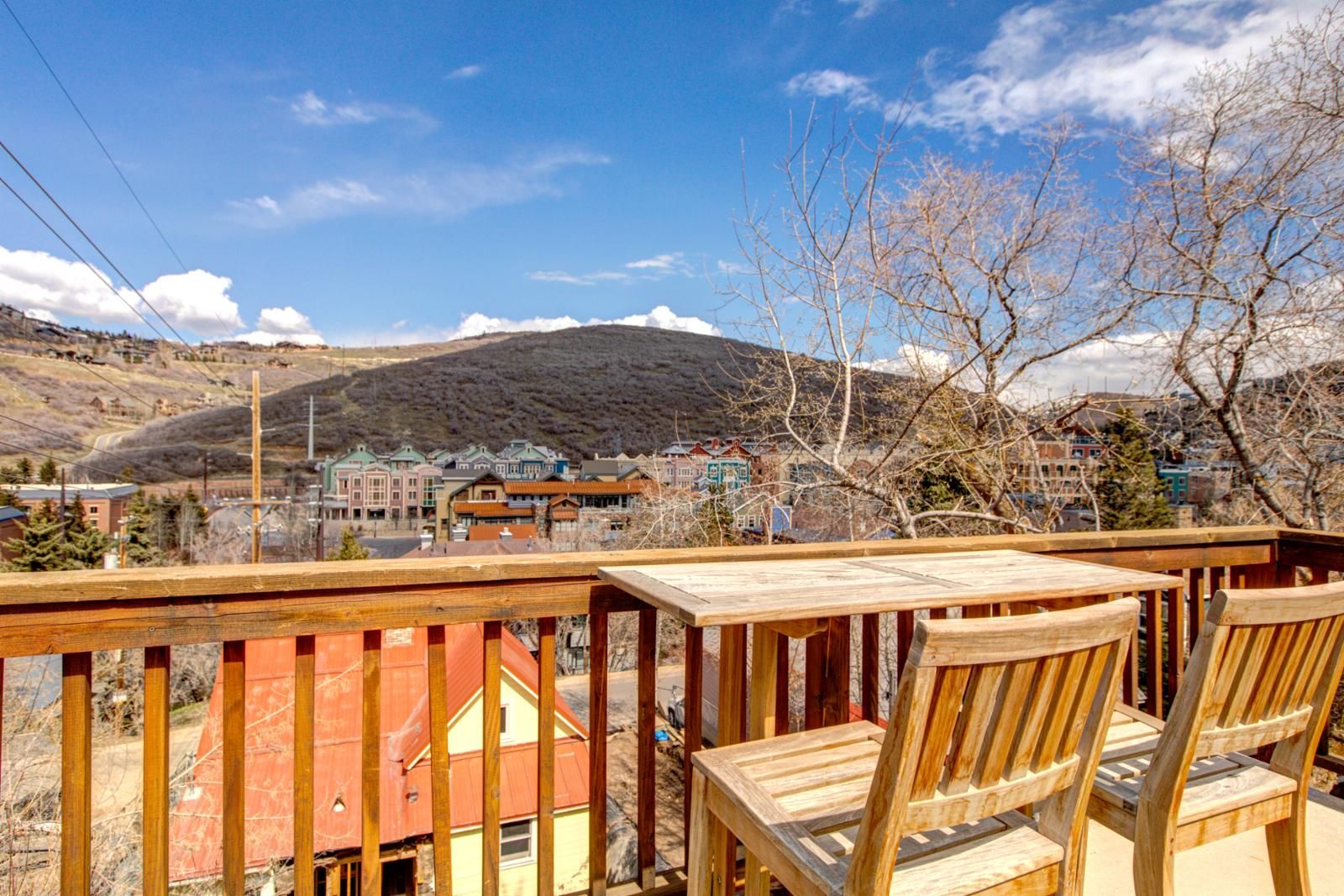 Une terrasse en bois avec des chaises, d’où l’on peut admirer une ville avec ses bâtiments et une montagne en arrière-plan.