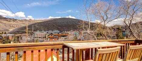 Une terrasse en bois avec des chaises, d’où l’on peut admirer une ville avec ses bâtiments et une montagne en arrière-plan.