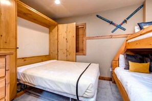 Un dormitorio con una cama litera, una cama individual, paredes de madera y un soporte para esquíes.