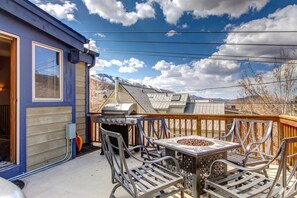 Una terraza con una parrilla y sillas de metal, con vistas a un paisaje montañoso.