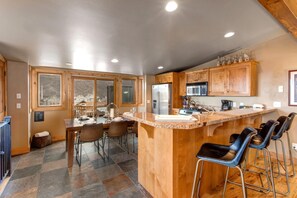Una cocina con encimera de granito, electrodomésticos de acero inoxidable, armarios de madera y una zona de comedor con sillas y una mesa.
