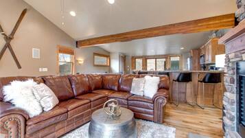 A spacious living room with a leather sectional sofa, a fireplace, and a kitchen area in the background.