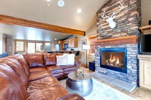 A living room with a stone fireplace, leather sofa, and a kitchen in the background. - KBM Resorts | Private Home | Split AC in living room | Walk to Town and to Ski Access, Hot Tub and Fire Pit! PNF-860 (Park City)