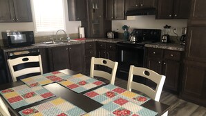 Une cuisine avec des meubles en bois foncé, un four à micro-ondes, un grille-pain et une cuisinière. On y trouve une table recouverte d’une courtepointe aux couleurs vives, ainsi que deux chaises.