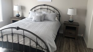 Une chambre à coucher avec un lit, deux tables de chevet avec des lampes, un tableau encadré au mur et un plancher en bois.