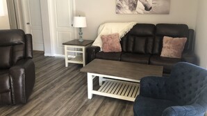 Un salon avec un canapé en cuir marron foncé, un fauteuil bleu, une table basse blanche et une lampe sur une table d’appoint.