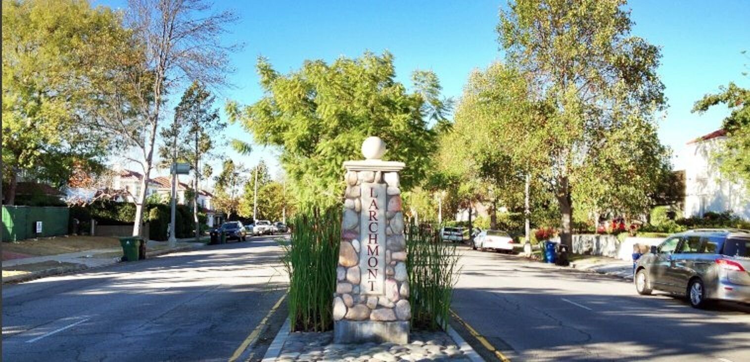 A stone monument with the inscription "LARSON MONT" in a residential street with cars and trees.