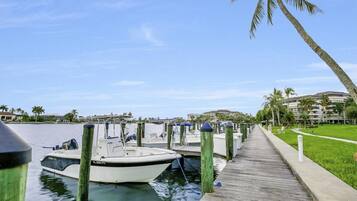 A marina with boats docked, a wooden walkway, and palm trees.