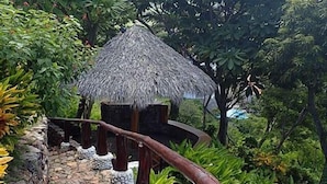 A thatched-roof structure on a stone pathway surrounded by lush greenery.