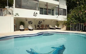 Una casa moderna de dos pisos con piscina, mobiliario exterior y detalles decorativos en las paredes.