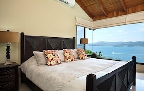 Un dormitorio con una cama grande, cabecera de madera y vistas al mar.