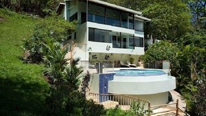 Una casa moderna de dos pisos con piscina rodeada de abundante vegetación.