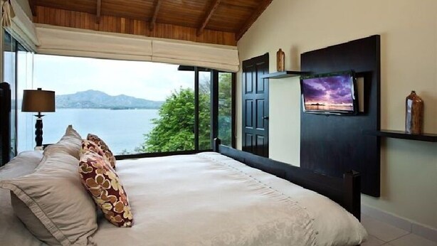 Un dormitorio con una cama grande, un televisor montado en la pared y vista a un lago.