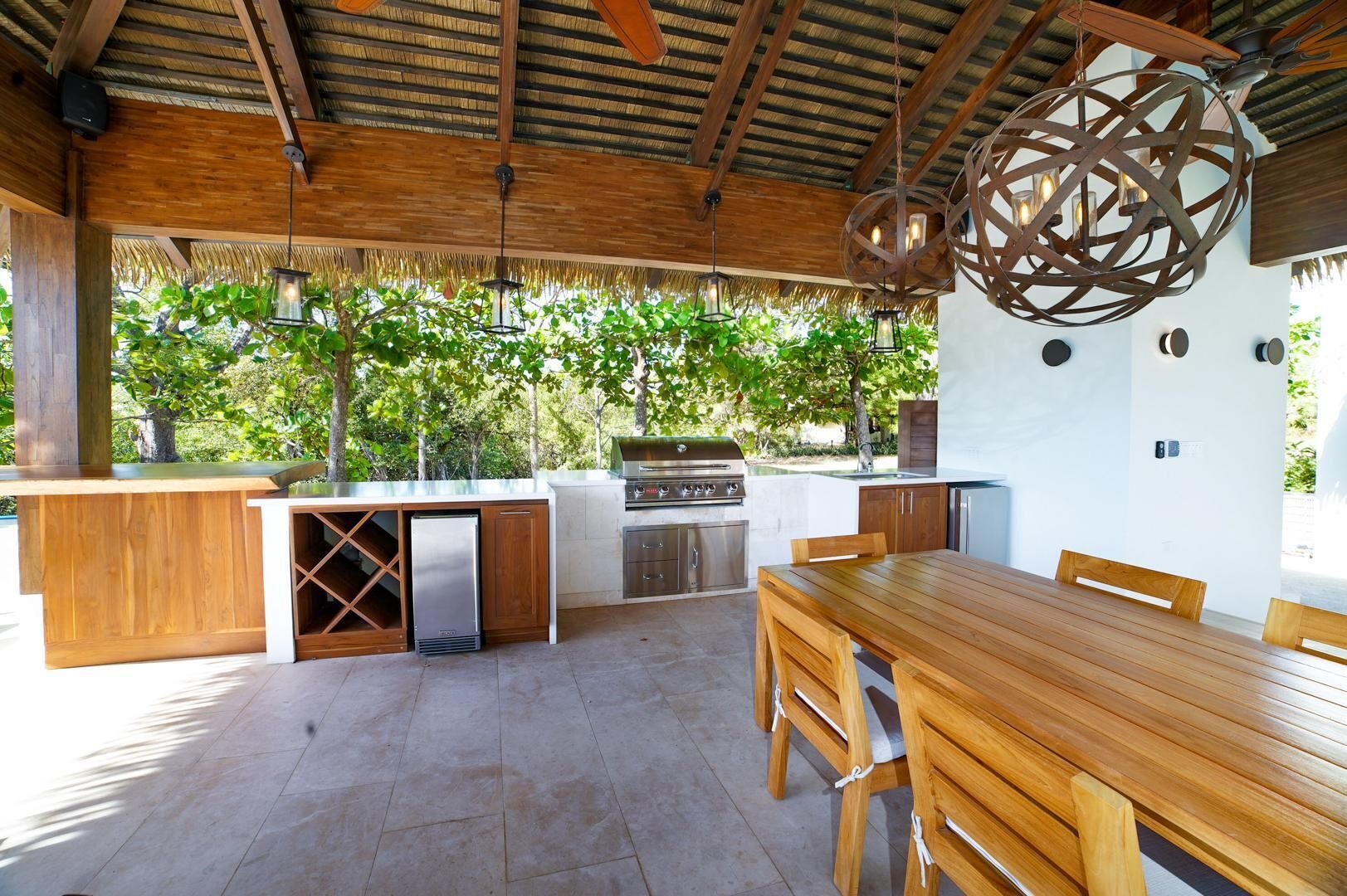 An outdoor kitchen area with a wooden table and chairs, a grill, and a wine cooler.