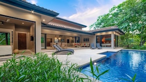 Una casa moderna con piscina, area salotto esterna e patio coperto.