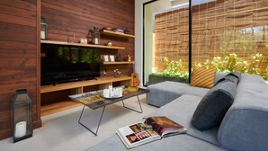 Una sala de estar moderna con un televisor de pantalla plana grande, estanterías de madera, una mesa de centro de vidrio y un sofá con una revista.
