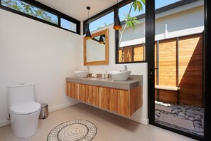 A modern bathroom with a wooden vanity, two vessel sinks, a toilet, and a large mirror.