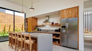 Una cocina moderna con armarios de madera, un refrigerador de acero inoxidable y una zona de bar con taburetes de madera.