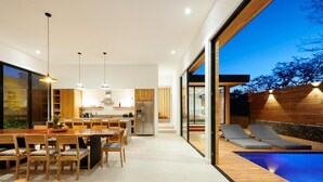 Una cocina moderna con armarios de madera, un comedor con mesa y sillas de madera, y una zona de piscina con sillas de descanso.