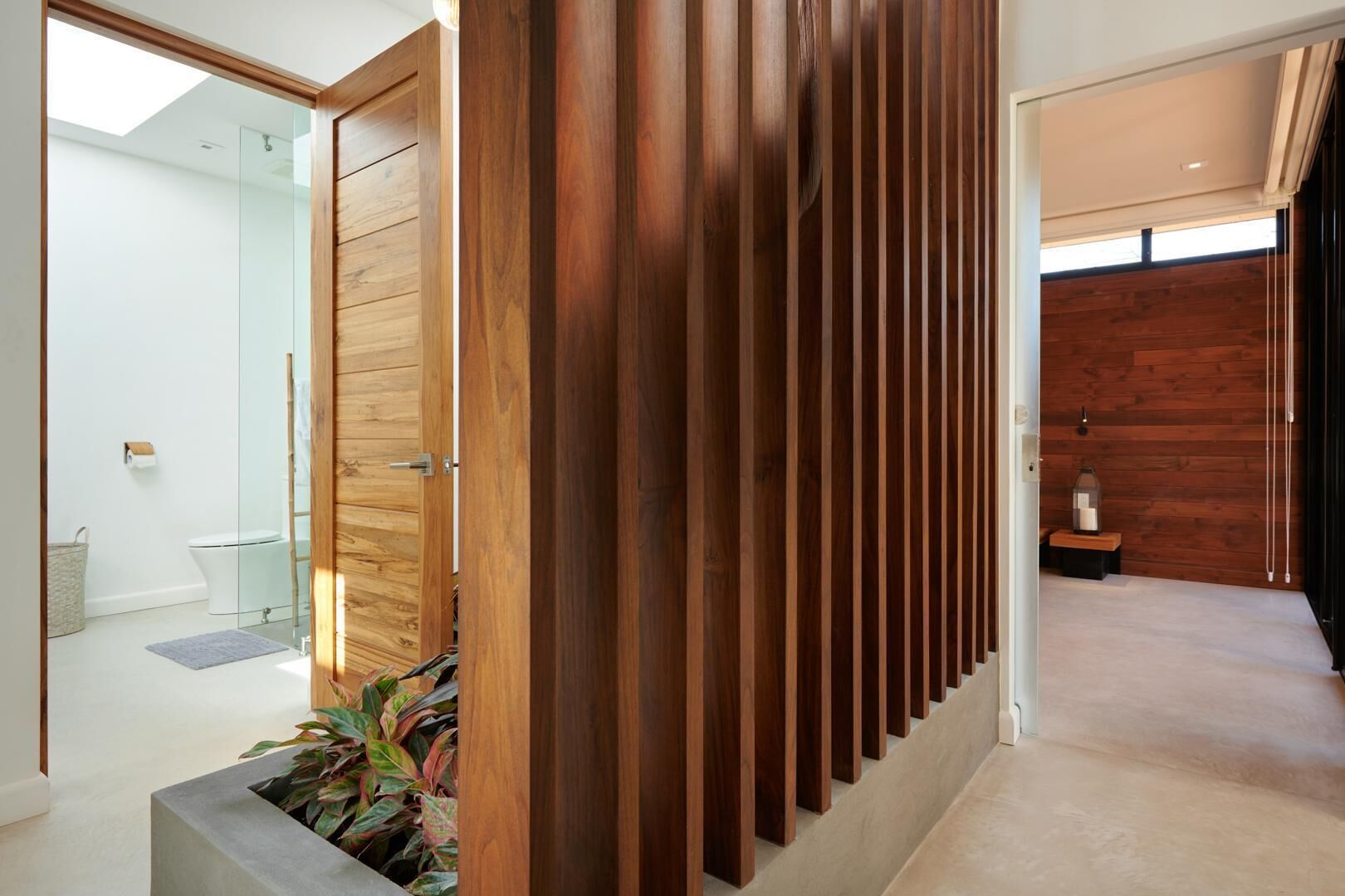 A modern interior with a wooden slat partition, a glass shower enclosure, and a hallway leading to a wooden wall.