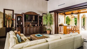 Un salon spacieux avec un grand canapé beige, un meuble de rangement en bois et une plante en pot.