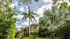 Un chemin menant à un bâtiment doté d’un toit en tuiles, entouré d’une végétation luxuriante et de palmiers.