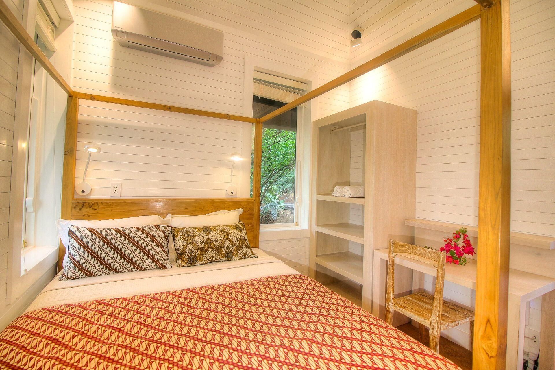 Une chambre à coucher comprenant un lit, des lampes de chevet, une fenêtre, une chaise en bois et une armoire intégrée.
