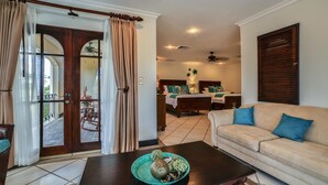 A living room with a sofa, a coffee table with decorative items, a dining area with a table and chairs, and a bedroom with two beds. - Villa Tranquila (Tamarindo)