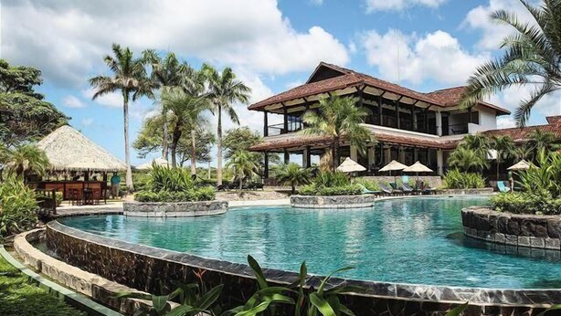 A resort with a large pool, palm trees, and a building with a thatched roof. - Villa Tranquila (Tamarindo)