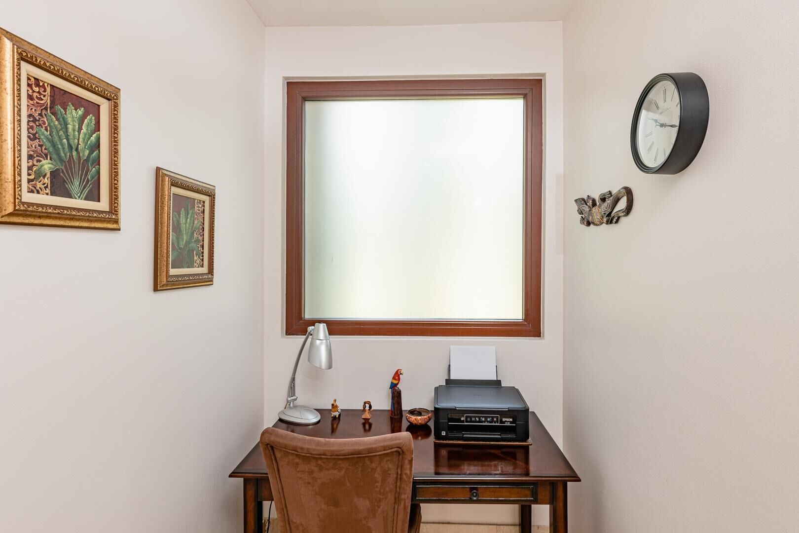 A study with a large window, a desk with a printer, a lamp, and framed artwork on the wall.