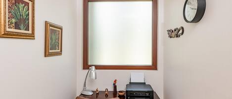 A study with a large window, a desk with a printer, a lamp, and framed artwork on the wall.