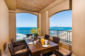 A dining area with a table set for two, overlooking a beach with clear blue waters and distant mountains. - Crystal Sands 504 (Tamarindo)