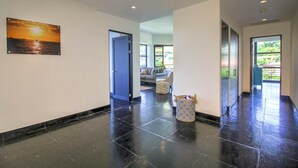 A hallway with a black tiled floor, a painting of a sunset, and a view into a living area with a sofa and a basket.