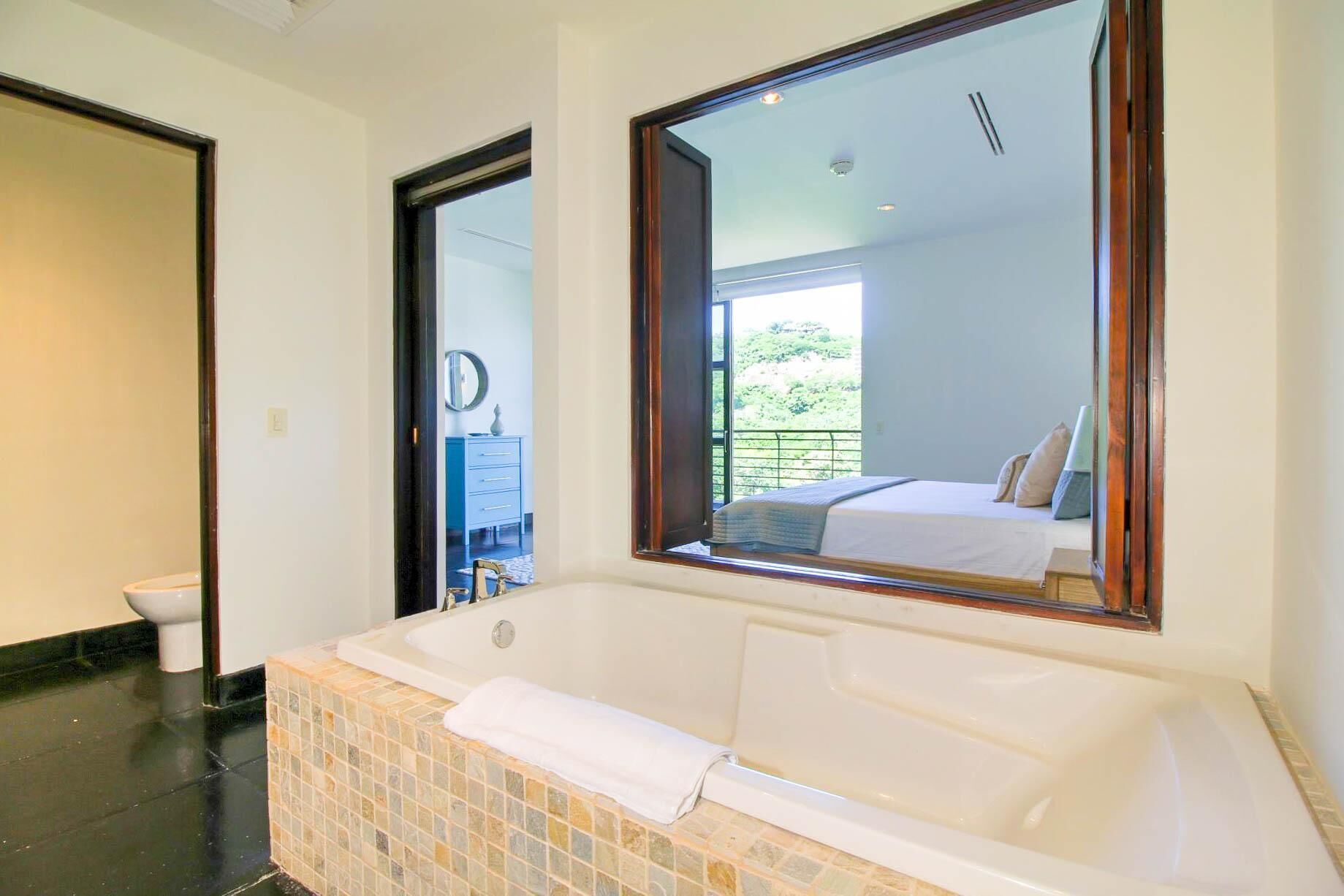 A bathroom with a large bathtub, a toilet, and a mirror.